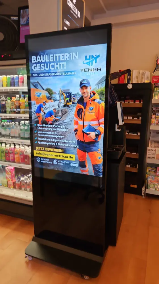A floor-standing commercial-grade screen inside a shop, playing a local business's ad